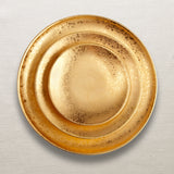 Textured Gold Alchimie Dining Set stacked on top of a woven beige tablecloth.