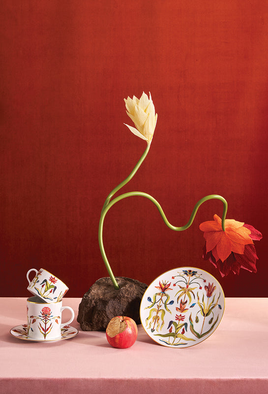 Decorative items including a tulip, cups, and a plate on a pink surface with a red background