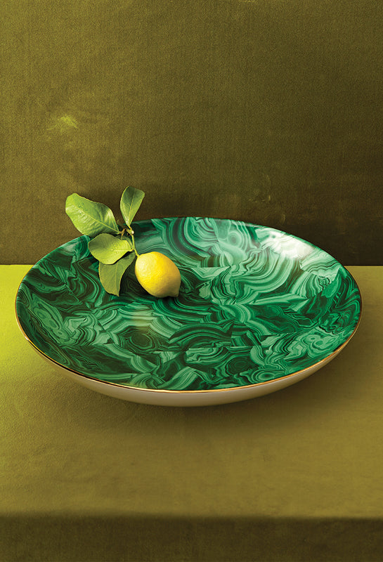 Green marbled dish with a lemon and leaves on a green surface