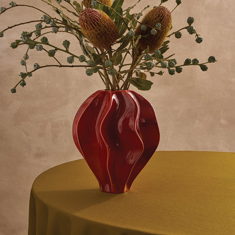 Red wavy vase with dried plants on a green surface against a beige background