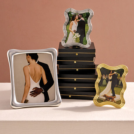 Three decorative photo frames with wedding images on a surface against a pink background