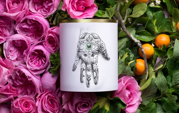 Porcelain candle vessel with illustrated hand in a bed of pink roses and orange branches.