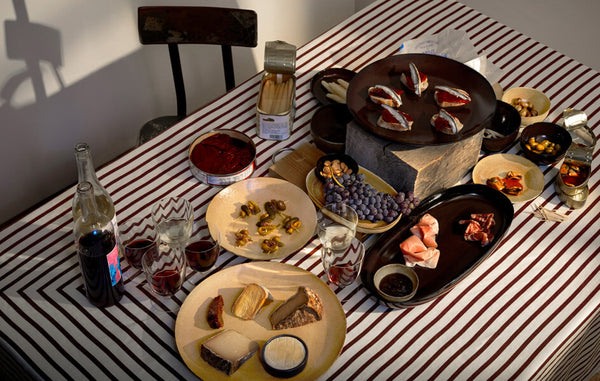 Tabletop set with leather and wine glazed Terra plates and platters, wine and ecru striped tablecloth.