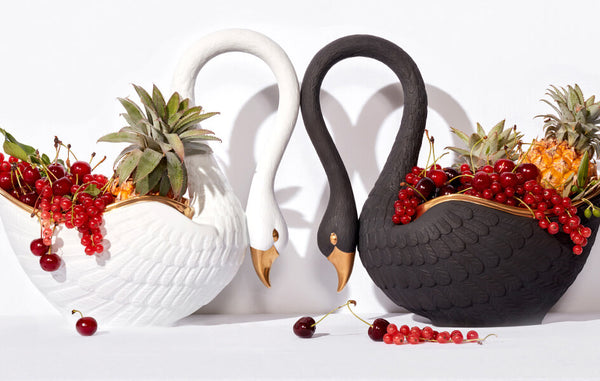 Porcelain black and white swan shaped bowls with sculpted feathers and gold details, filled with pineapples and berries.