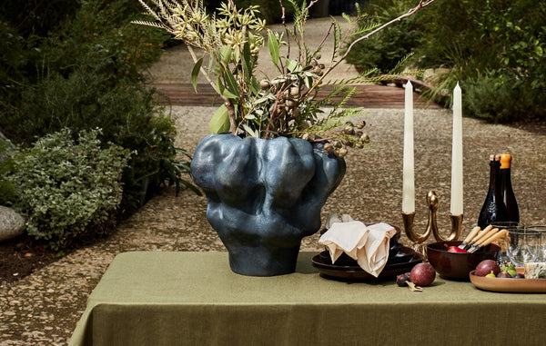 Outdoor tabletop set with a dramatic, scultped Timna vase glazed mineral blue and filled with branches.