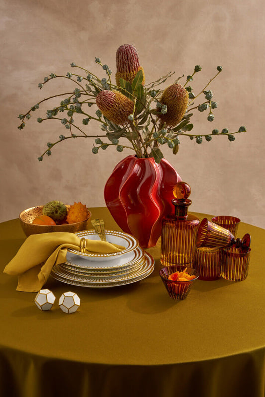 Dining table setting with plates, bowls, and decorative items on a yellow tablecloth.