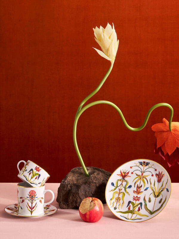 Decorative items including a tulip, cups, and a plate with floral designs on a pink surface against a red background.