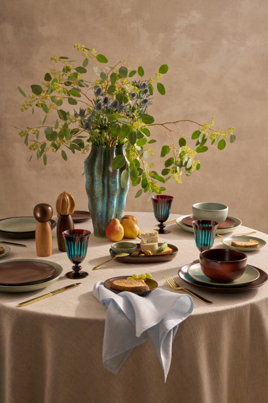 Dining table set with ceramic plates, glasses, and cutlery on a beige background