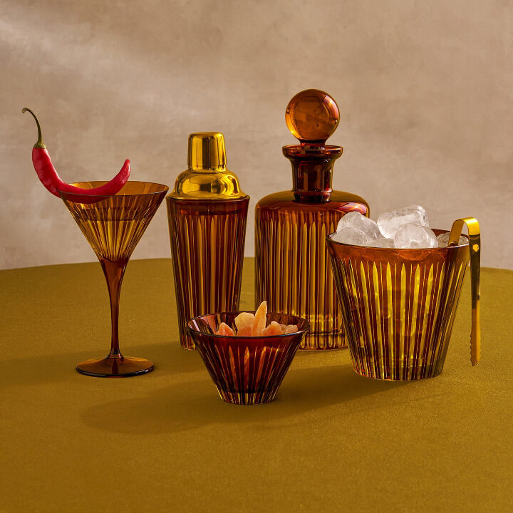 Set of bar tools including a martini glass, bottle, and ice bucket on a green surface with a neutral background.