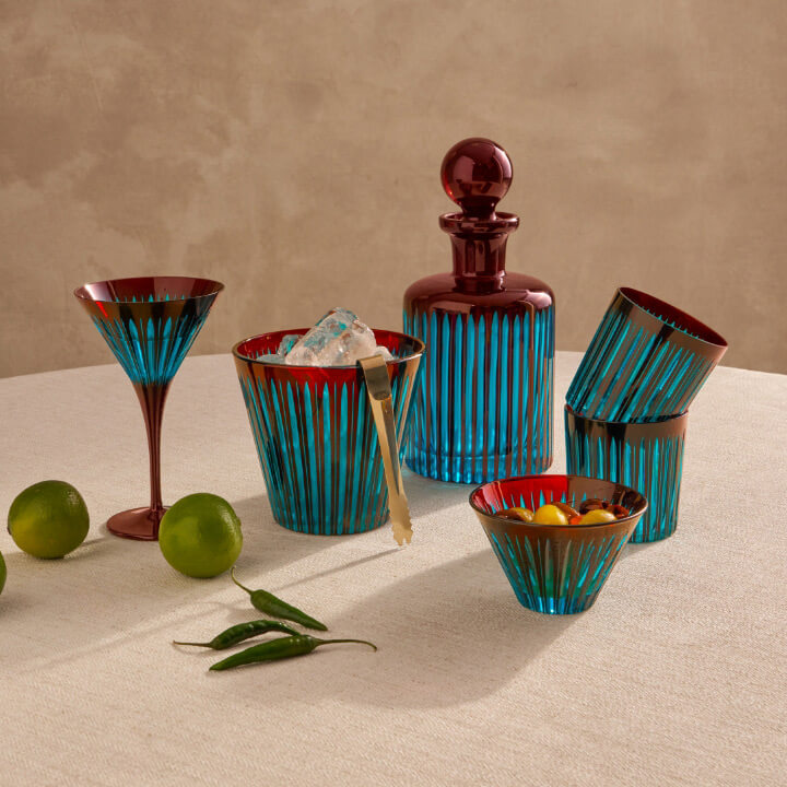 Set of bar accessories including glasses, decanter, and bowls on a textured surface with limes and peppers.