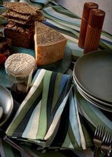 Tabletop with Natural wood ionic spice mills and Linen tablecloth and napkins with an organic, undulating pattern in blue, green and ivory hues.