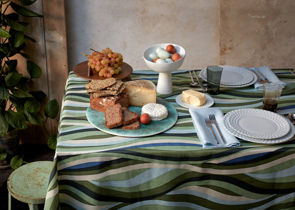 Table set with blue green landscape pattern tablecloth, Green round placemat, stone glazed terra bowl on stand, aegean white waves dinnerware